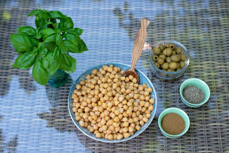 A set of ingredients for the preparation of hummus pesto with olives: chickpeas, spices, olive oil, fresh basil. Recipe for a vegetarian Mediterranean appetizer.の写真素材