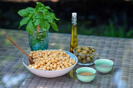 A set of ingredients for the preparation of hummus pesto with olives: chickpeas, spices, olive oil, fresh basil. Recipe for a vegetarian Mediterranean appetizer.の写真素材
