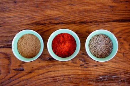 Oriental spices cumin, ground zira and red pepper paprika in bowls on a wooden oak table. Flat lay....