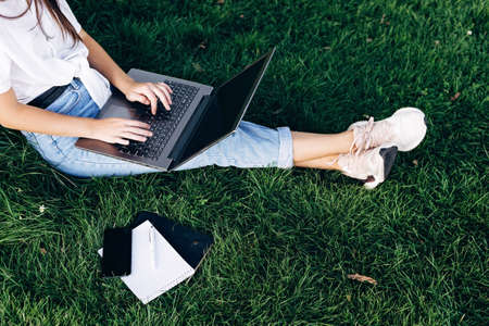student girl with laptop outdoors sitting on the grass, surfing the internet or preparing for exams....