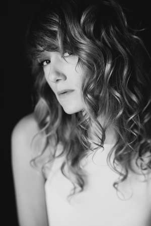 Portrait of a 36 year old woman with curly hair and brown slanting eyes. Soft selective focus. Black...