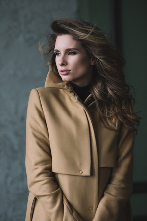 Beautiful sexy girl with curls and full lips in a beige coat in a loft style studio. Beauty and fashion. Soft selective focus.の写真素材