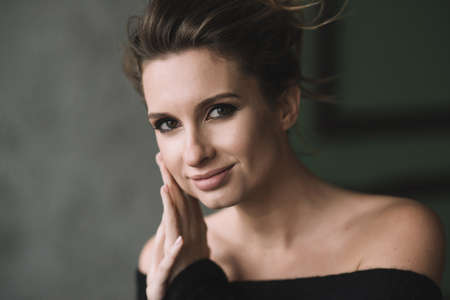 A beautiful girl with curls and full lips in a black sweater folded her hands near her face and...
