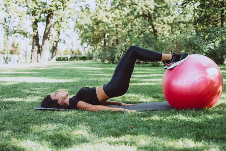 Young happy fit tanned brunette goes in for sports with a big fitness ball, dressed in active black...