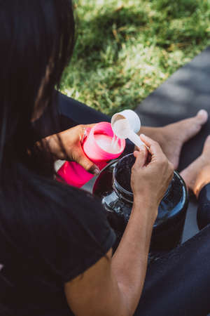 woman athlete prepares a protein shake in a shaker after training outdoors. Sports nutrition. Soft...