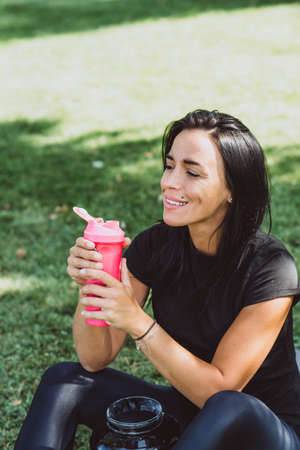 Young fit tanned woman athlete drinks protein shake after training outdoors. Sports nutrition. Soft...