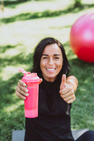 Young fit tanned woman athlete drinks protein shake after training outdoors. Sports nutrition. Soft selective focus.の写真素材