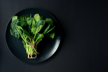 Clean food concept. Bunch of leaves of fresh organic spinach greens in a plate on a black background. Healthy detox spring-summer diet. Vegan Raw Food. Copy space.の写真素材