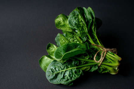 Clean food concept. Bunch of leaves of fresh organic spinach greens on a black background. Healthy detox spring-summer diet. Vegan Raw Food.の写真素材