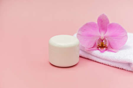 Jar of moisturizing body cream, bath towel, orchid flower on a pastel pink background. Skin care cosmetic concept. Soft selective focus. Copy space.の写真素材