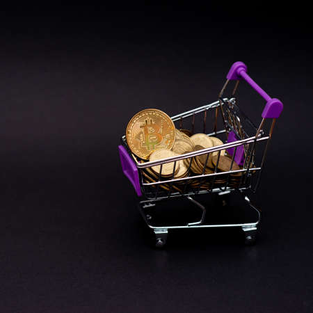 Bitcoin coins in a shopping cart. Virtual cryptocurrency purchase concept. Black background. Bitcoin...