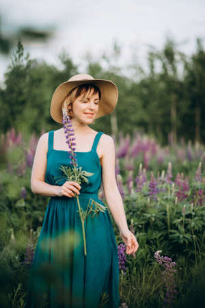 Beautiful romantic girl blonde in a hat and dress in a field of purple flowers of lupins with a...