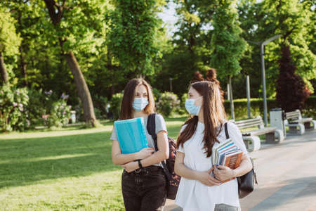 Two student girls in protective medical masks walk and talk on the campus. Distance education. Soft selective focus.の写真素材