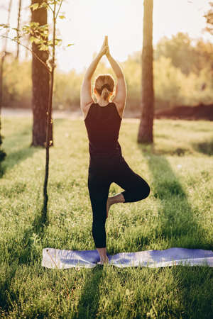 a 36 year old woman practices yoga on an early sunny morning in the woods among the trees. Healthy...
