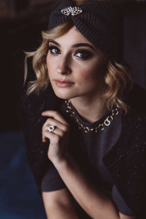 Portrait of a beautiful stylish blonde woman in a knitted headband in a loft interior. Soft...