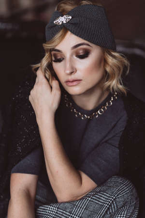 Portrait of a beautiful stylish blonde woman with smoky eye makeup in a knitted headband. Soft...