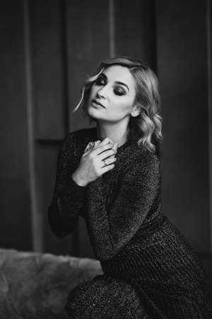 Portrait of a beautiful blonde woman in a black dress with smoky eye makeup in a loft interior. Soft...