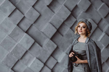 Beautiful stylish woman photographer in a gray outfit with a camera in her hands in a photo studio....