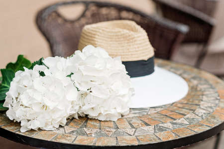 Lonely hat and white hydrangea flowers on a stone table. Romantic spring and summer background. Soft selective focus.の写真素材