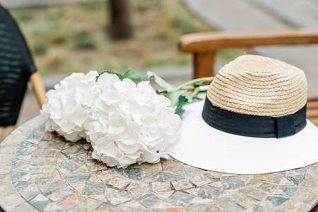 Lonely hat and white hydrangea flowers on a stone table. Romantic spring and summer background. Soft selective focus.の写真素材