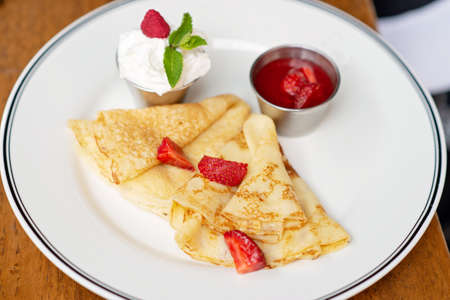 Delicious crepes with fresh strawberries, mint leaves and sour cream espuma. Breakfast at the restaurant. Soft selective focus.の写真素材