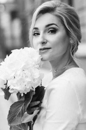 Portrait of a beautiful woman with an elegant hairstyle in a white jacket and hydrangea flowers in her hands. Soft selective focus.の写真素材