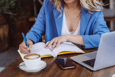 Beautiful woman freelancer, blogger, influencer with laptop works remotely and drinks coffee. A photographer as a hobby. Soft selective focus.の写真素材