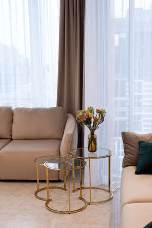 Glass round bedside table with gold with a vase of flowers in a modern beige interior. Interior Design. Soft selective focus, artistic noise.の写真素材