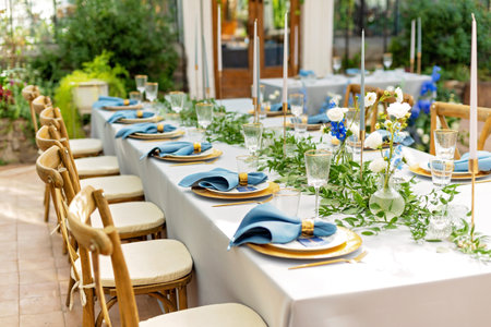 Banquet wedding table setting with blue napkins, gold cutlery, crystal, fresh flowers and candles. Wedding decorations. Soft selective focus.の写真素材