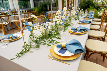Banquet wedding table setting with blue napkins, gold cutlery, crystal, fresh flowers and candles....