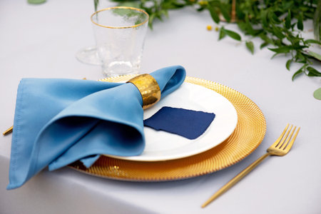 Elegant and chic wedding table setting in gold and blue colors and fresh flowers. Soft selective...