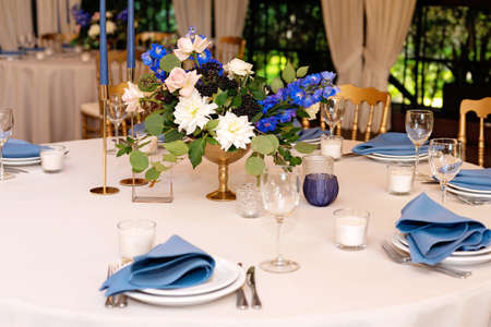 Festive wedding, table setting with blue linen napkins, candles and fresh flower bouquets. Wedding decorations. Restaurant menu concept. Soft selective focus.の写真素材