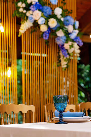 Wedding presidium, banquet table for newlyweds with flowers, greenery, blue and gold color. Lush flower arrangement on the wedding table. Glowing light bulbs. Soft selective focus.の写真素材