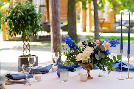 Festive wedding, table setting with blue linen napkins, candles and fresh flower bouquets. Wedding...