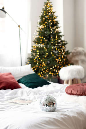 Christmas decor. Bedroom in light colors with a large bed. The interior is decorated with garlands, Christmas wreaths and a New Year tree in a modern style. Soft selective focus.の写真素材