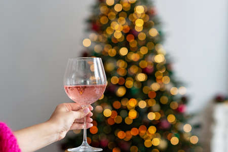 Glass of champagne rose in hand against the background of bokeh lights of the Christmas tree. Winter holiday. New year background. Soft selective focus.の写真素材