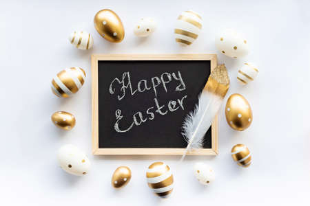 Gold white eggs and feather on a white background. Minimal concept. View from above. Easter card with the inscription happy easter in a frame. Soft selective focus.の写真素材