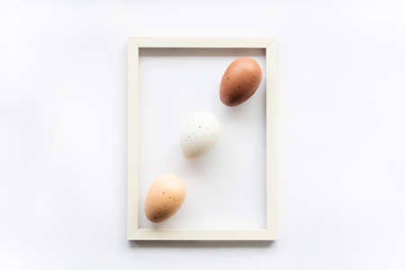 Three natural eco eggs on a white background with copy space for text in a frame. Geometry. Minimal concept. View from above. Easter card, soft selective focus.の写真素材