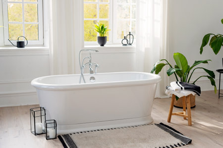 Stylish modern bathroom interior. Horizontal view of an empty free-standing bathtub on a wooden floor in a bright room against the backdrop of a large window and houseplants. Soft selective focus.の写真素材
