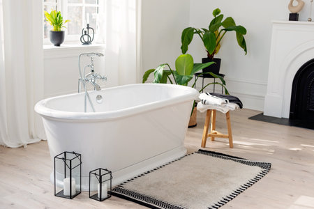 Stylish modern bathroom interior. Horizontal view of an empty free-standing bathtub on a wooden floor in a bright room against the backdrop of a large window and houseplants. Soft selective focus.の写真素材