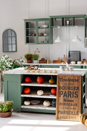 Kitchen with green vintage furniture, marble countertop with flowers and pumpkins, pots of autumn flowers, cupboard with various mugs, crockery and cutlery. Vertical. Soft selective focus.の写真素材