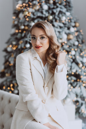 Young happy european businesswoman wearing glasses sitting at workplace with decorated Christmas tree behind, smiling woman working in home office during winter holidays. Soft selective focus.の写真素材