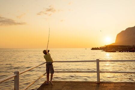Teenager boy catching the fish from the pier at sunset, Black Sea, Crimeaの写真素材