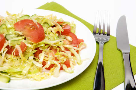 Cabbage salad with tomato and cucumber in white plate, knife and forkの写真素材