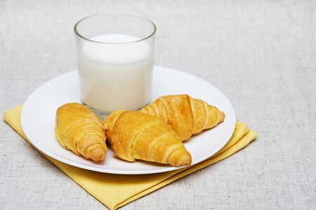 five croissants in a white plate with glass of milk on a beige backgroundの写真素材