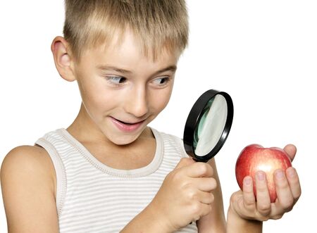 Boy  looking through a magnifying glass on apple in his hand. Isolated on white.の写真素材