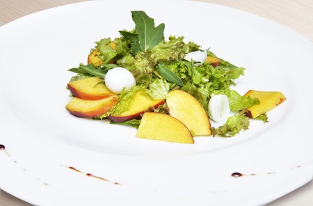 Salad with peaches and mozzarella cheese on white plateの写真素材