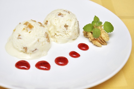 vanilla ice cream with pieces of pear, walnut and strawberry jam on white plateの写真素材