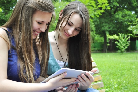 two young girls using a tablet computer outdoor in parkの写真素材