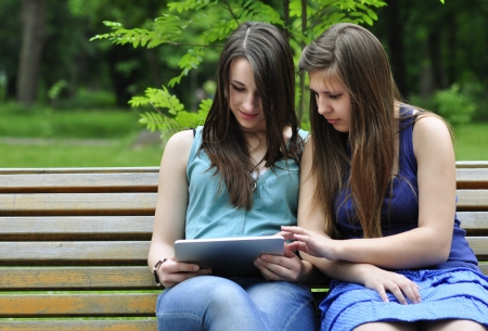two young girls on bench using a tablet computer outdoor in parkの写真素材